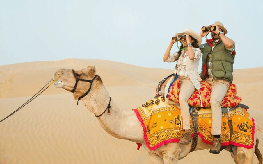 Two people riding a camel in a desert. 3