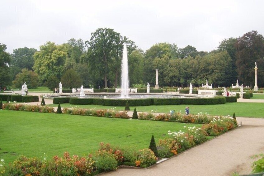 A well-manicured park with a central fountain, neatly trimmed hedges, and a variety of flowers. 3