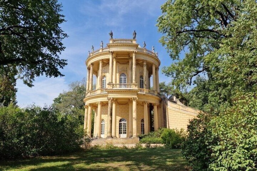 A classical building with columns, a dome, and statues, surrounded by lush greenery. 2