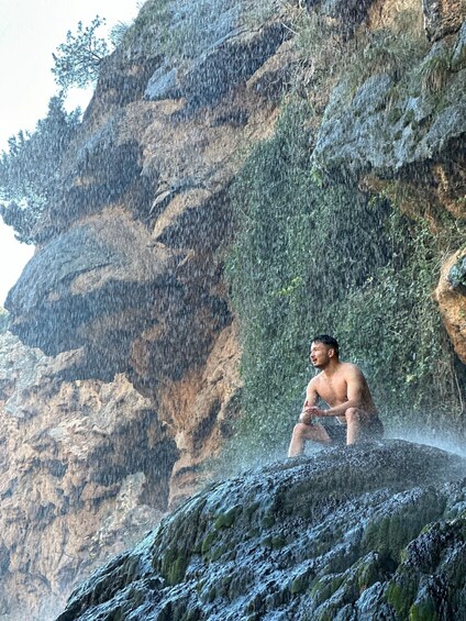 A man sitting on a rock in a mountainous area with rain falling. 3