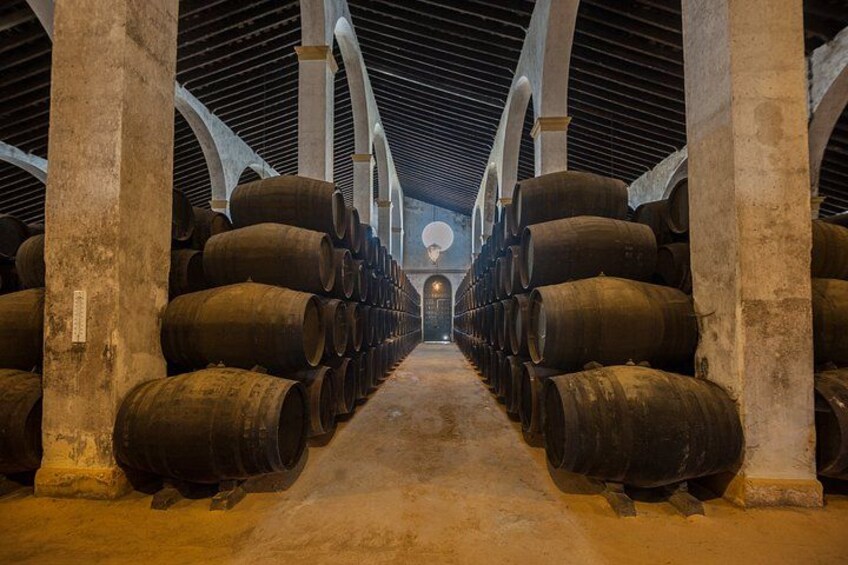 A warehouse with rows of large barrels, arched ceiling, and a central aisle leading to a door. 3