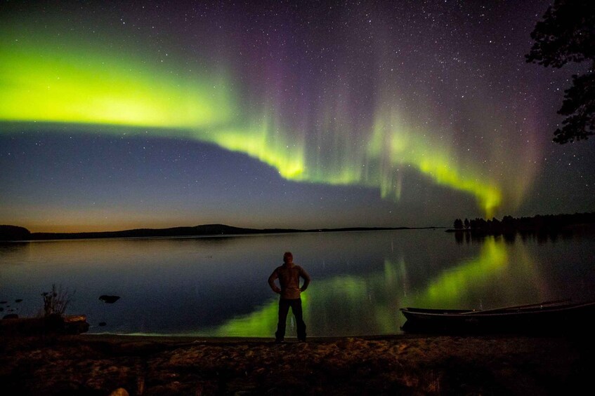 A person standing by a calm lake at night, with the Northern Lights in the sky. 2