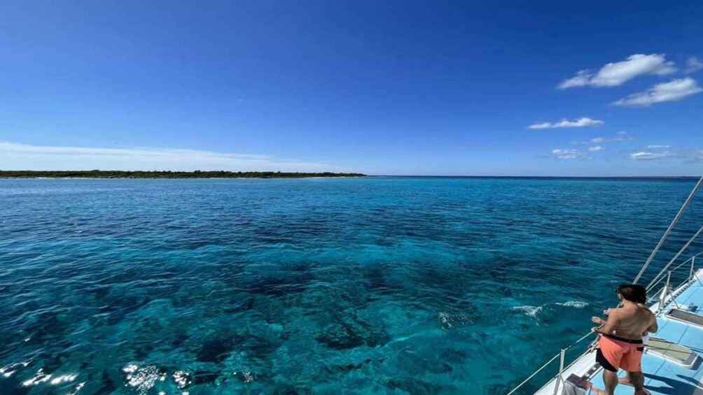 A clear blue sea, a person on a boat, and a distant shoreline. 4