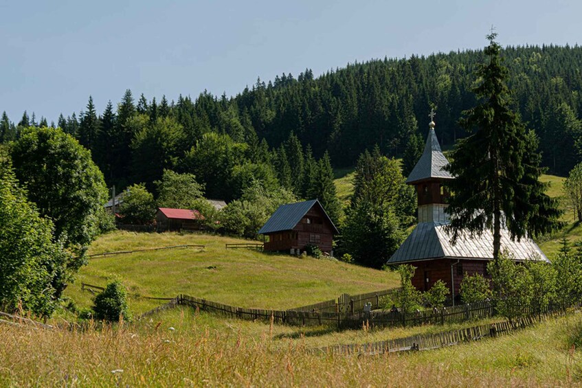 A rural landscape with a church, a wooden house, and a forested hill. 2