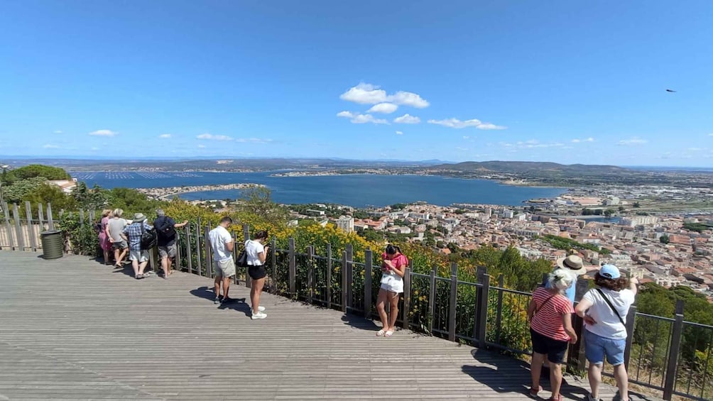A wooden viewing platform with people overlooking a coastal city and a bay. 1