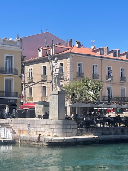 A statue in a public square with buildings and a body of water in the foreground. 2
