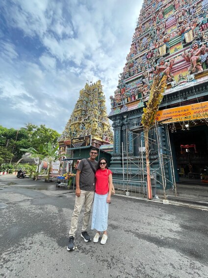 A temple with intricate carvings and statues, a person in a red shirt, and another in a grey shirt. 2