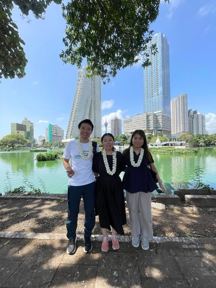 Three people standing by a lake with a cityscape in the background. 3