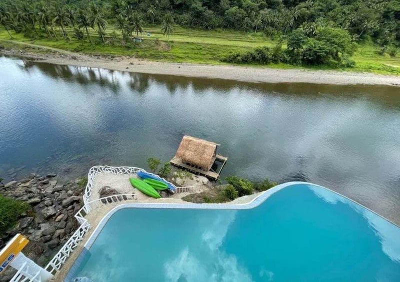 A swimming pool with a thatched-roof hut and a green kayak by the water's edge. 1