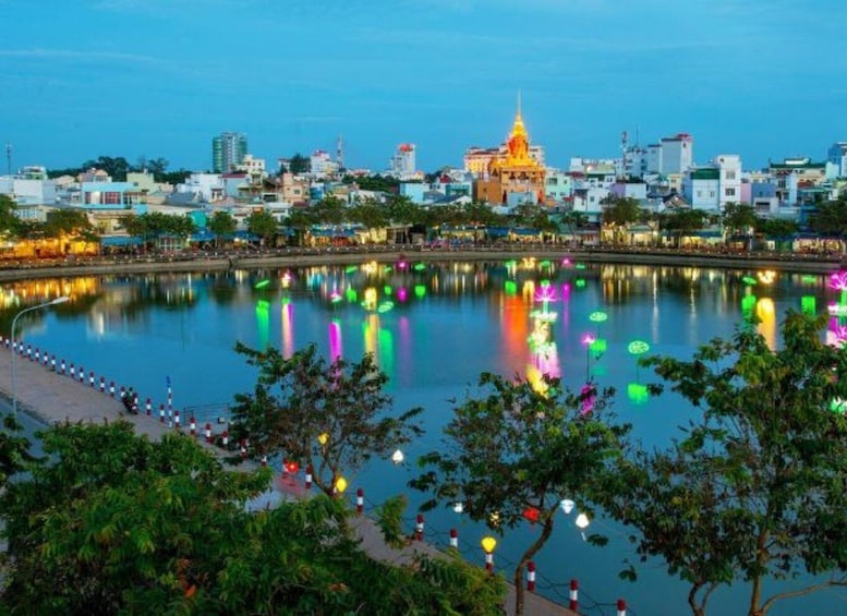 A cityscape with a prominent golden-domed building reflecting on a calm body of water, surrounded by colorful lights and greenery. 3