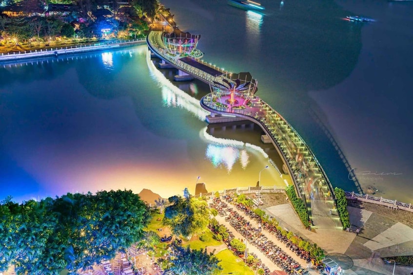 A riverside promenade with a curved bridge, seating areas, and a waterfront. 1