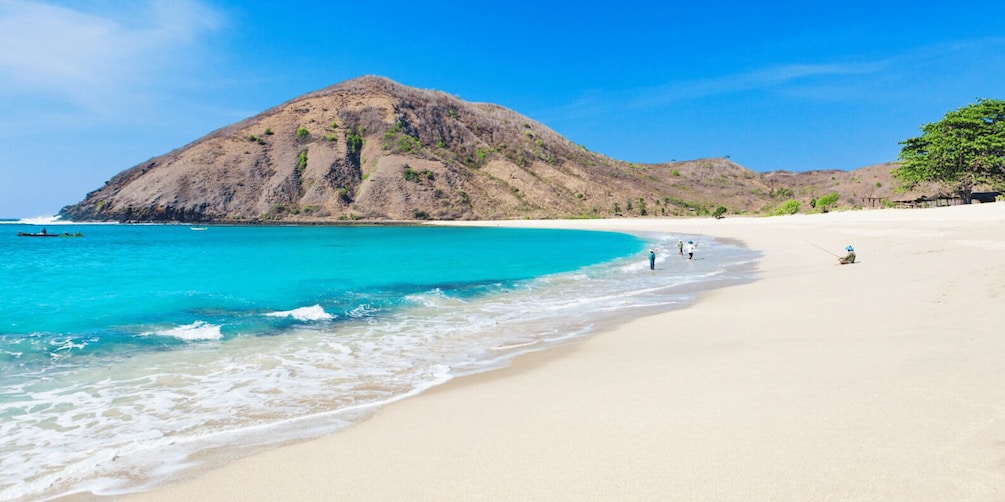 A beach with clear turquoise water, a sandy shore, and a large hill in the background. 1