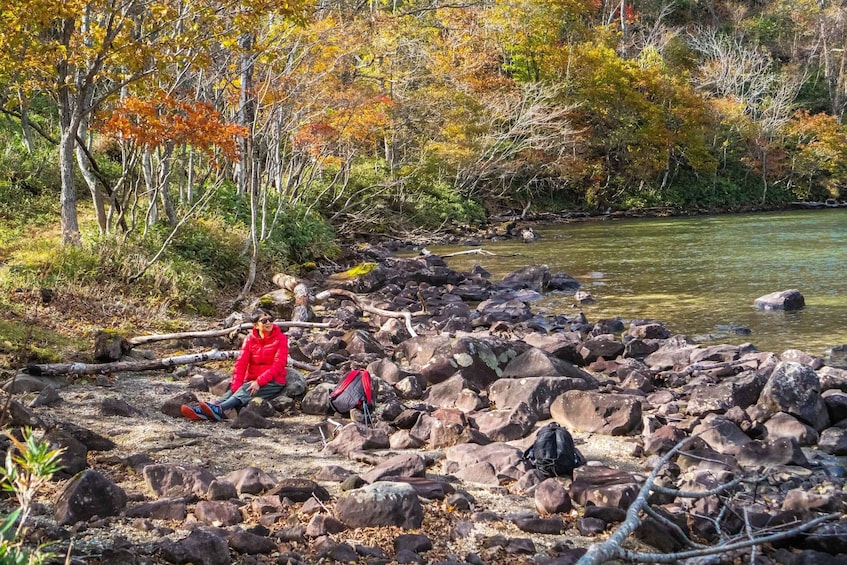 A rocky riverbank with autumn foliage and a person sitting on the rocks. 1