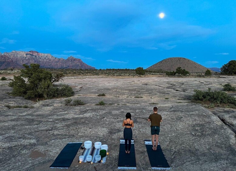 Two people on yoga mats in a rocky outdoor setting with a mountain in the background. 4