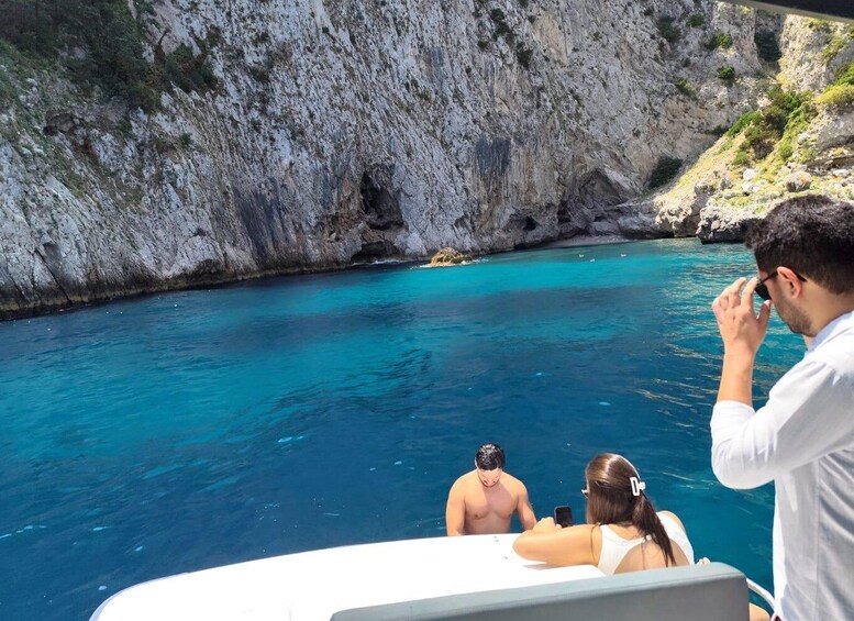 A boat with people taking photos of a rocky coastline and clear blue waters. 3