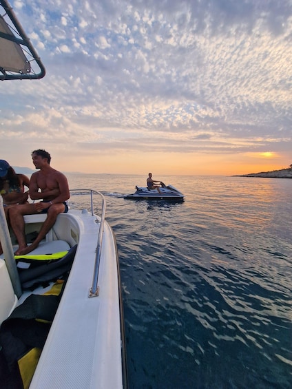 A boat with people and a jet ski on the water during sunset. 1