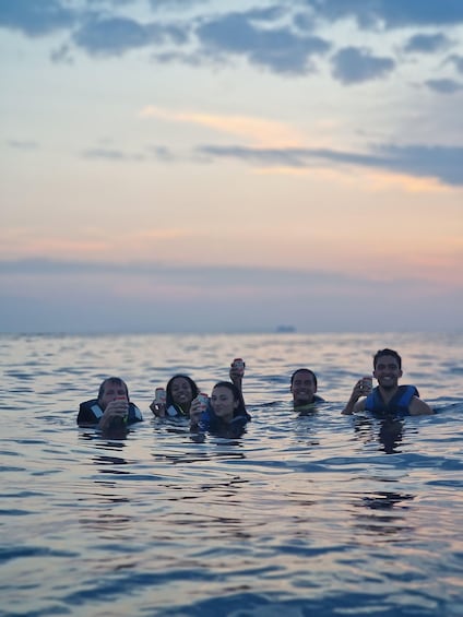 A group of people in a body of water during sunset. 5