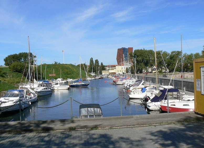 A marina with various boats docked, a wooden fence, and a tall building in the background. 3