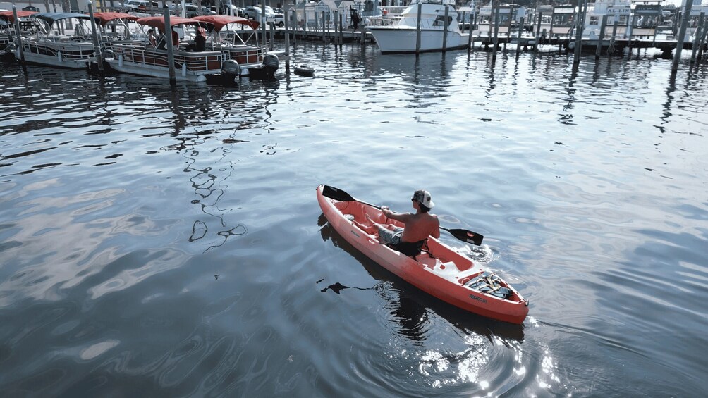 A person kayaking on calm water with boats docked in the background. 2