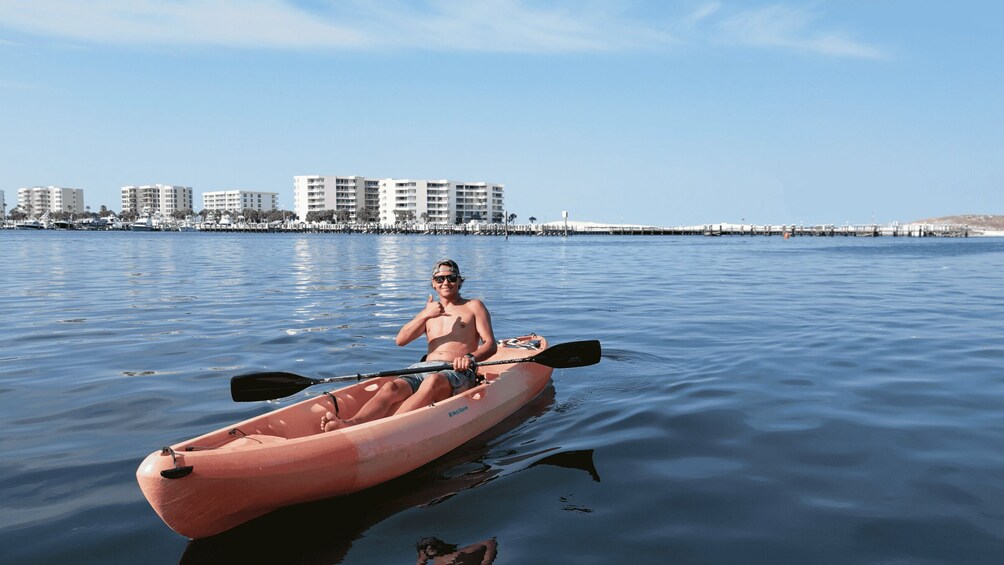A person kayaking on calm water with buildings in the background. 1