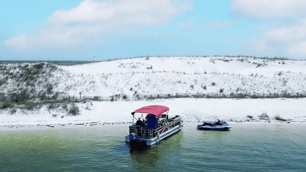 A boat with a red canopy on a calm body of water, a jet ski nearby, and a snow-covered hill in the background. 3