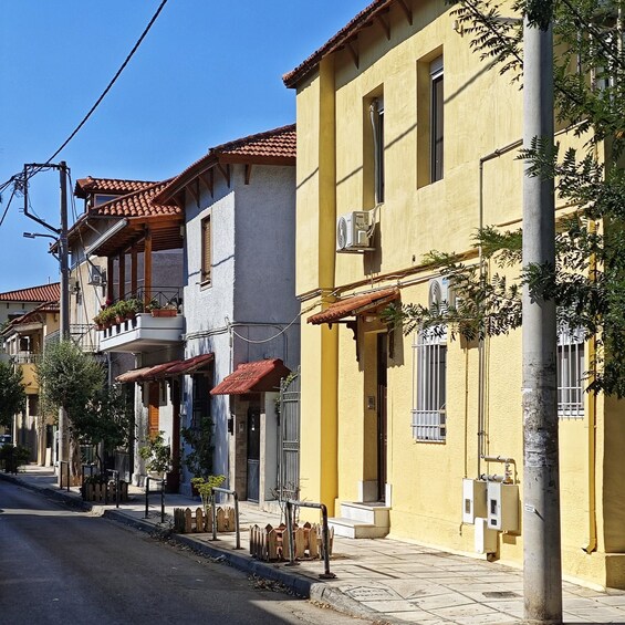 A row of Mediterranean-style buildings with red-tiled roofs, a clear blue sky, and a sidewalk with a wooden fence. 1
