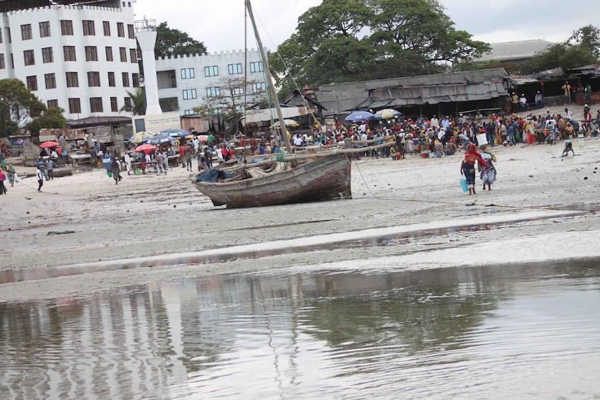 A crowded beach with people, a boat, and buildings in the background. 2