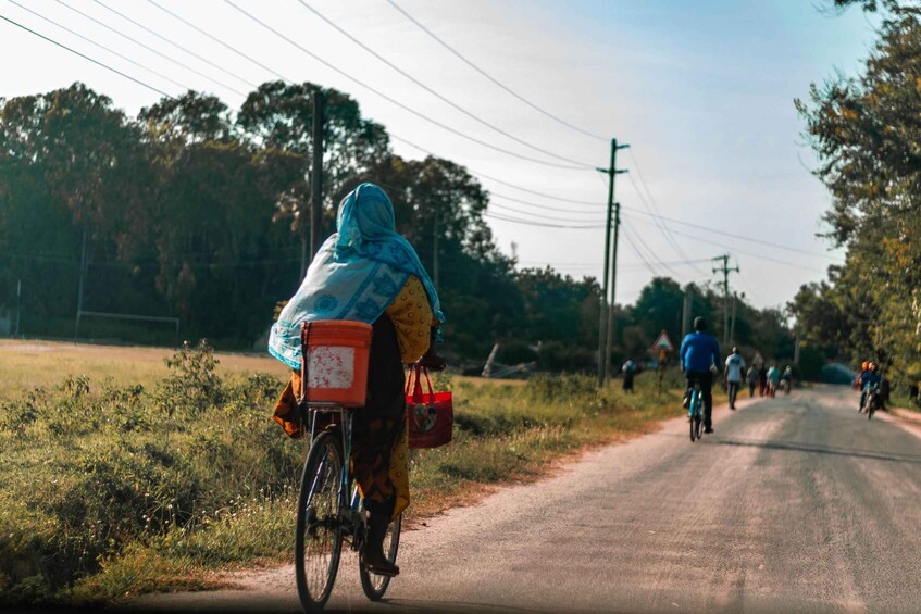 A person riding a bicycle on a rural road with other cyclists in the background. 5