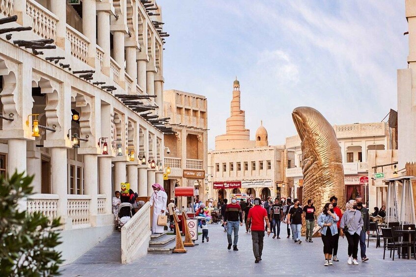 A bustling street with traditional architecture, a prominent golden spiral sculpture, and a mosque with a tall minaret in the background. 1