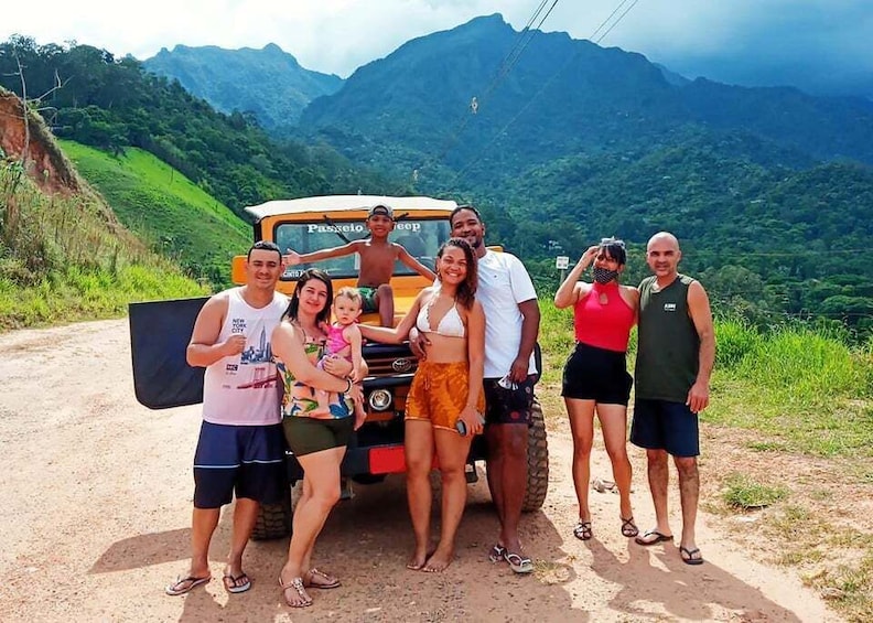 A group of people posing in front of a vehicle on a dirt road with a mountainous landscape in the background. 5