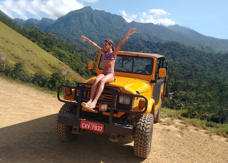 A person sitting on a yellow off-road vehicle with a license plate CXV-7937, surrounded by a mountainous landscape. 1