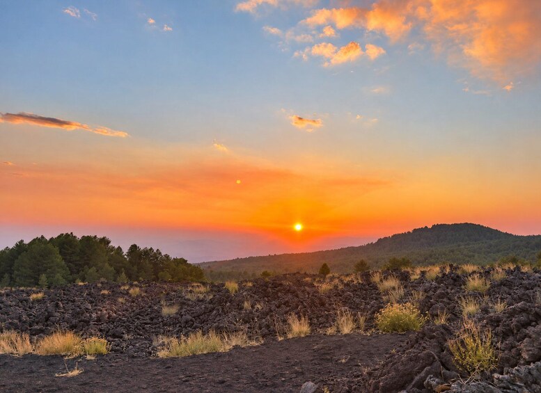 Solnedgang over et vulkanlandskab med sparsom vegetation. 3