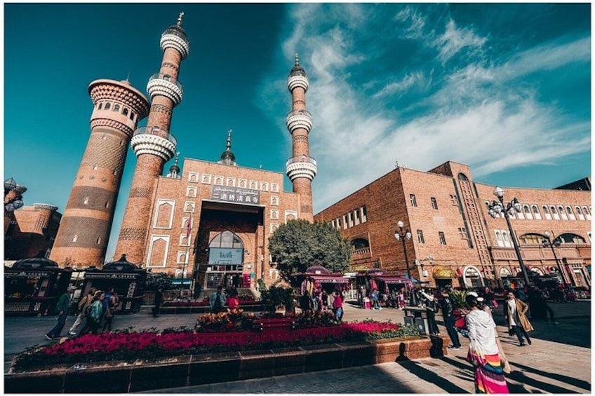 A mosque with three minarets, a large entrance, and a flower garden in front. 5