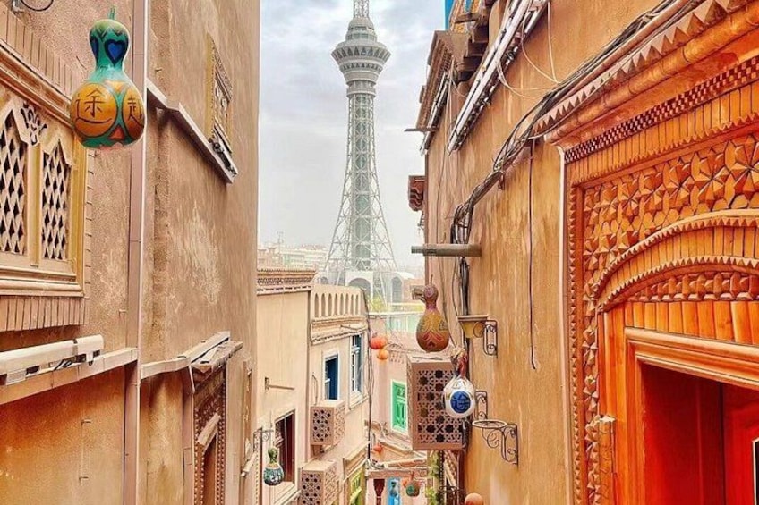 A narrow alleyway with ornate doors and windows, a tower in the background, and a red door on the right. 2