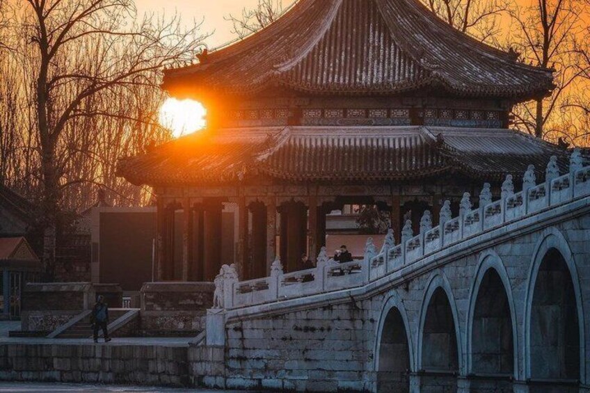A traditional Chinese pavilion with a tiled roof, a stone bridge with arches, and a sunset in the background. 5