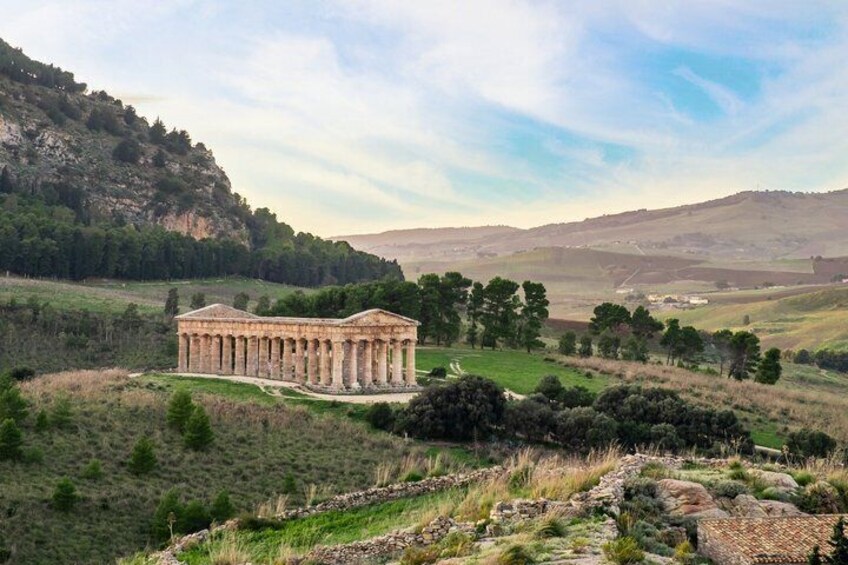 A classical temple with columns, set in a hilly landscape with trees and a clear sky. 2