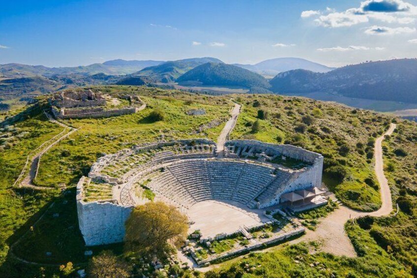 An ancient amphitheater surrounded by lush green hills and mountains. 1