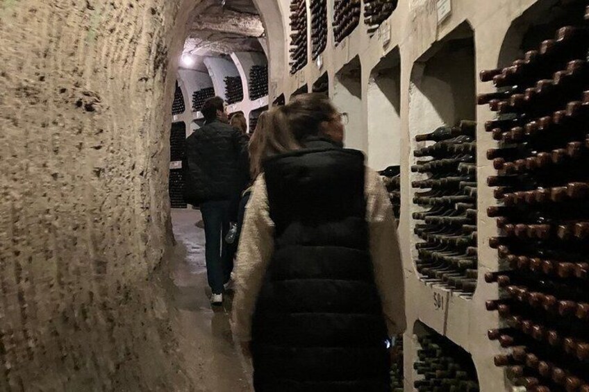 A narrow passage with stone walls and rows of wine bottles on shelves. 5
