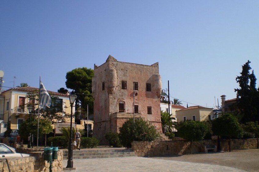 A historic stone building with a square base and a flat roof, surrounded by trees and modern buildings. 3