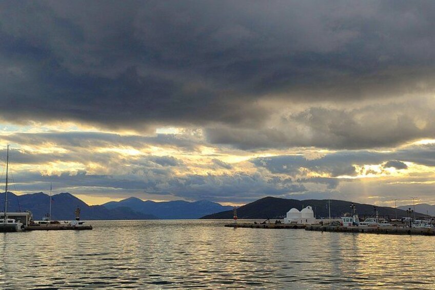 A coastal scene with a body of water, a white building, and mountains in the background under a cloudy sky. 2