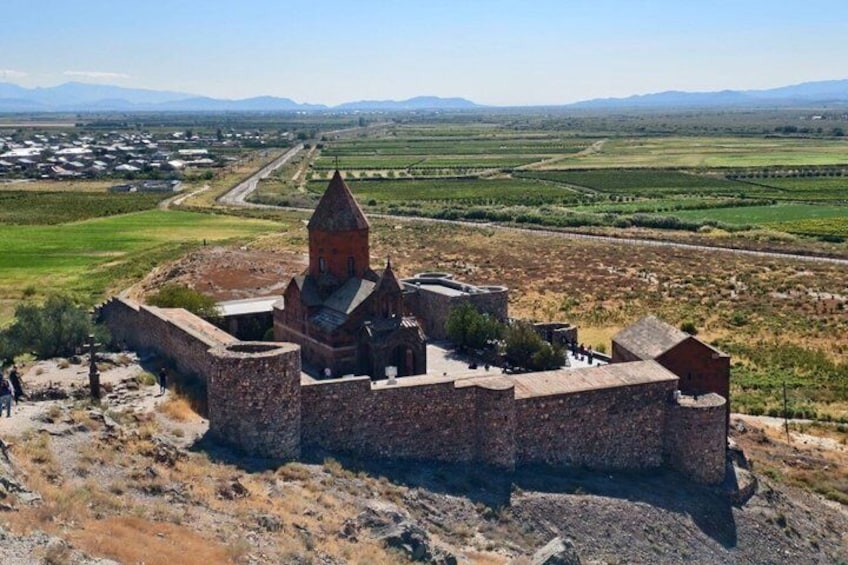 A historical stone fortress with a central tower, surrounded by a dry, hilly landscape. 1
