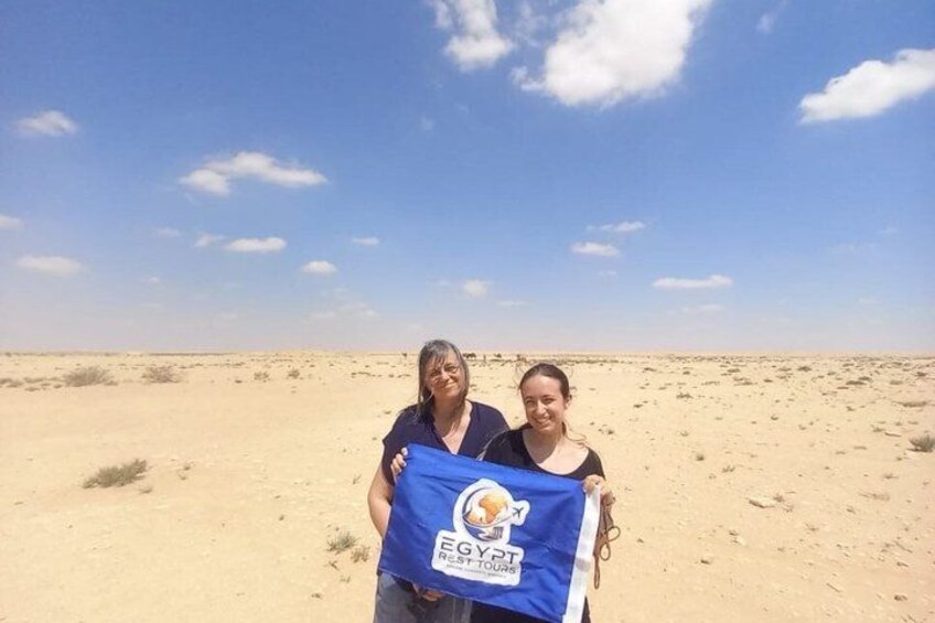 Two people holding a blue flag with 'EGYPT' and 'EGYPT TOUR' on it, standing on a sandy desert landscape. 4