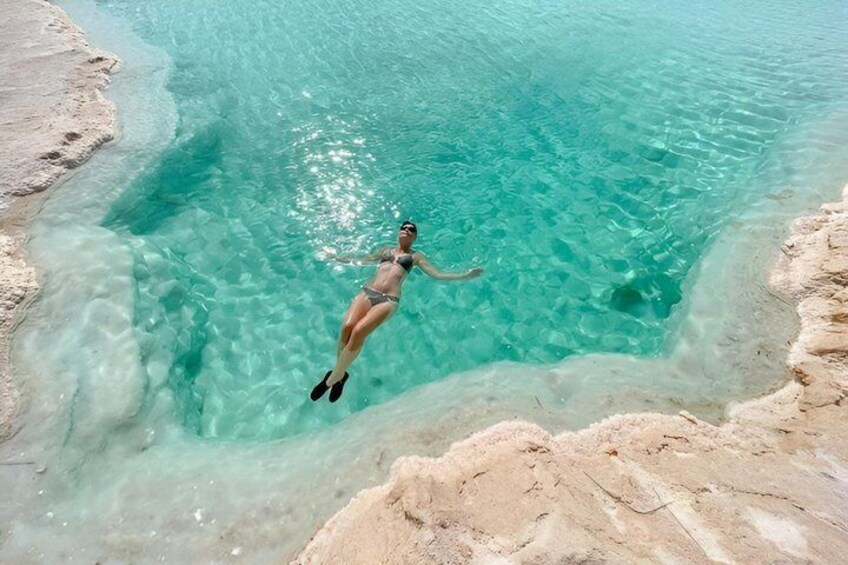 A person swimming in clear turquoise water with rocky edges. 3