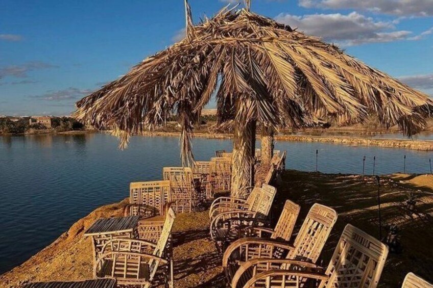 A thatched-roof structure with chairs by a body of water. 4