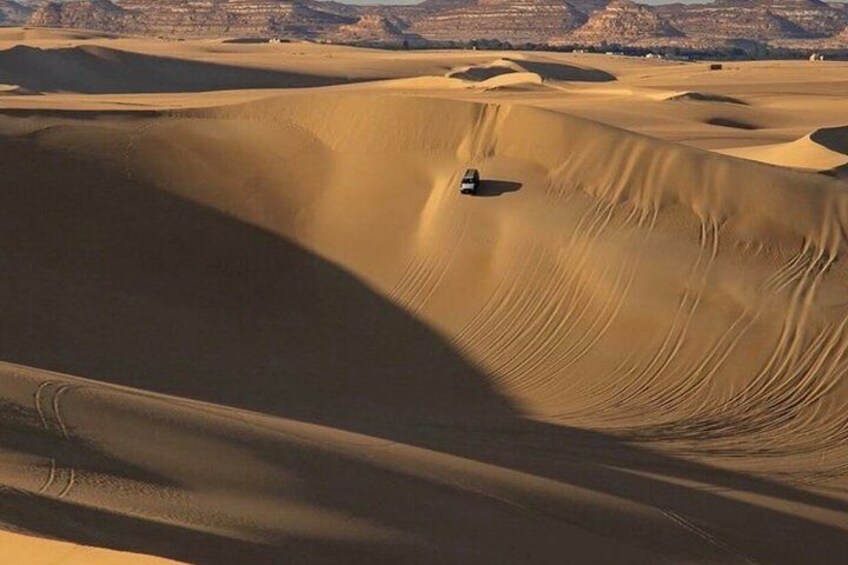 A desert landscape with undulating sand dunes and a vehicle navigating the terrain. 2