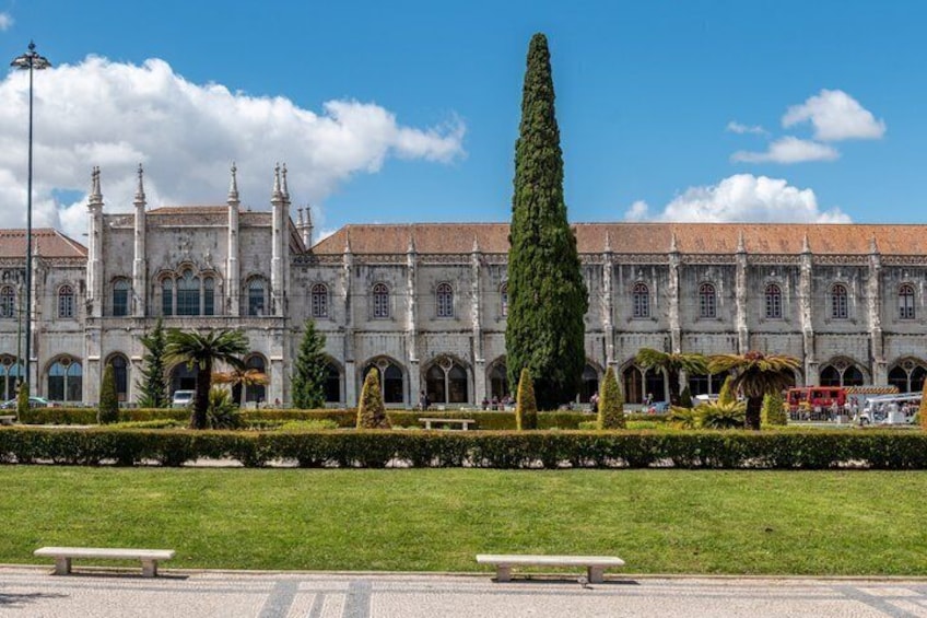 A historic building with arched windows and a central tower, surrounded by a well-manicured lawn and a red bus in the background. 3