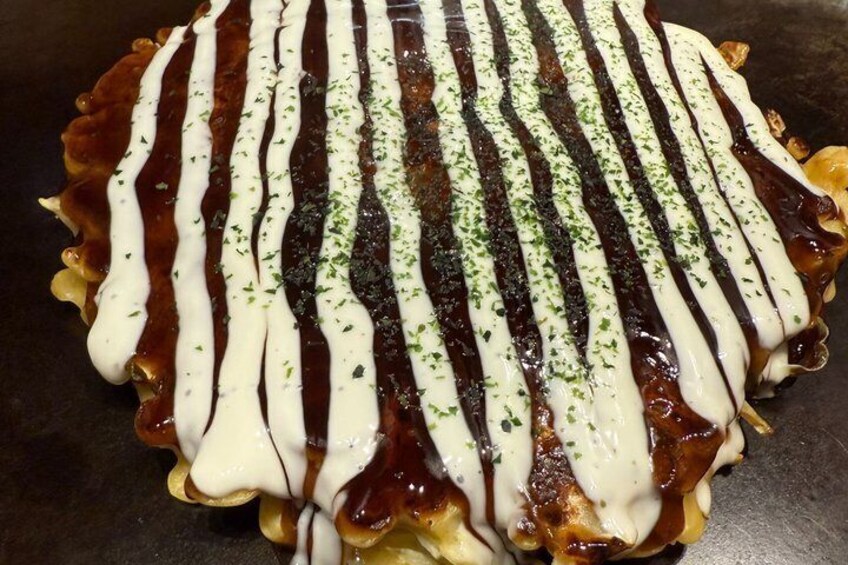 A large, round, deep-fried dish with white and dark sauces drizzled in lines and sprinkled with green herbs. 5