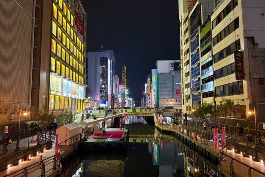 A nighttime cityscape with illuminated buildings, a canal, and a pedestrian bridge. 4