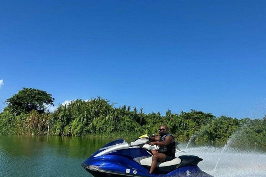 A person jet-skiing on a body of water with dense greenery in the background. 1