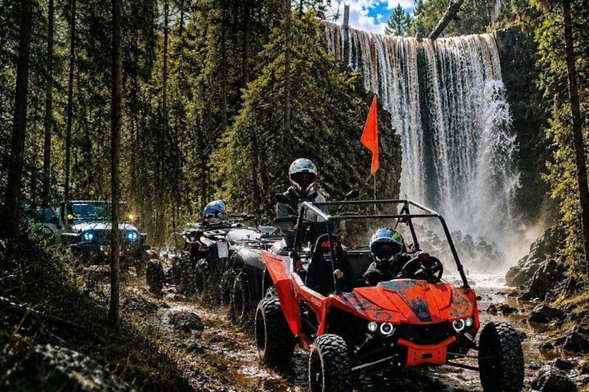 Off-road vehicles on a muddy trail with a waterfall in the background. 3